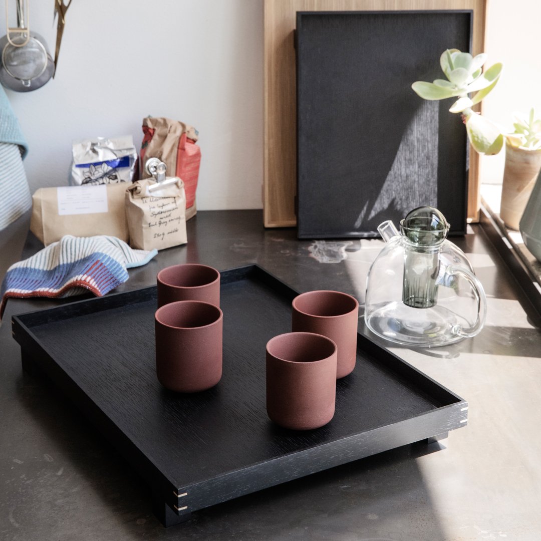 Rustic black tray with four maroon cups on a dark countertop, featuring natural textures and a minimalist aesthetic.