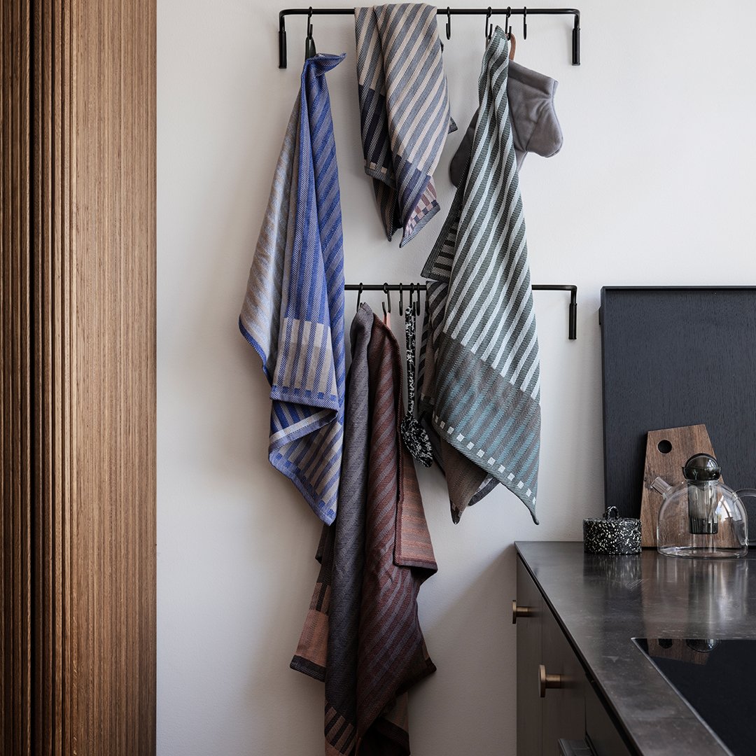 "Collection of striped kitchen towels in blue, gray, and brown hues, hanging on a rack against a modern backdrop."