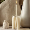Cream-colored taper candles in a clear holder against neutral backgrounds, featuring soft textures and minimalist design.