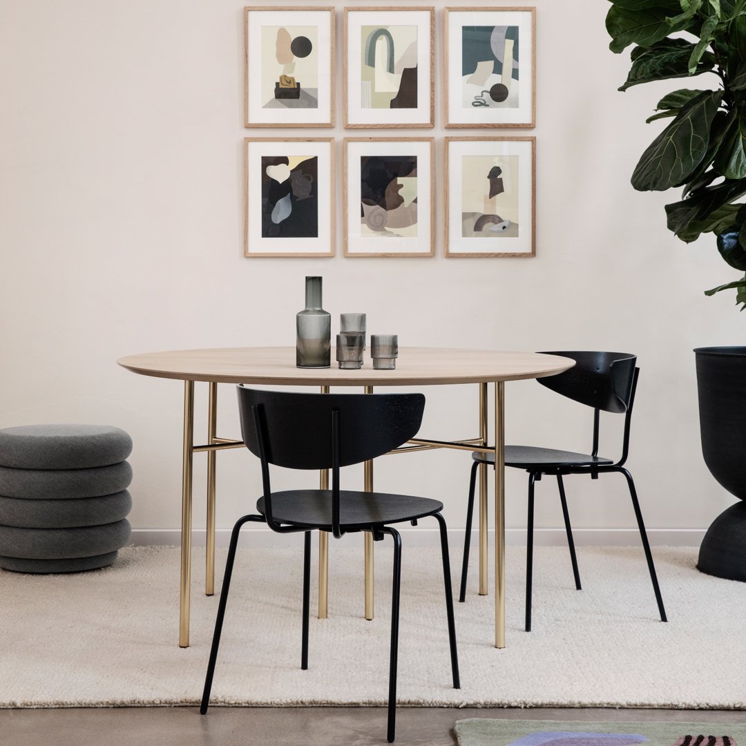 Minimalist round table with natural wood finish, black chairs, and a neutral rug, accented by framed art on the wall.
