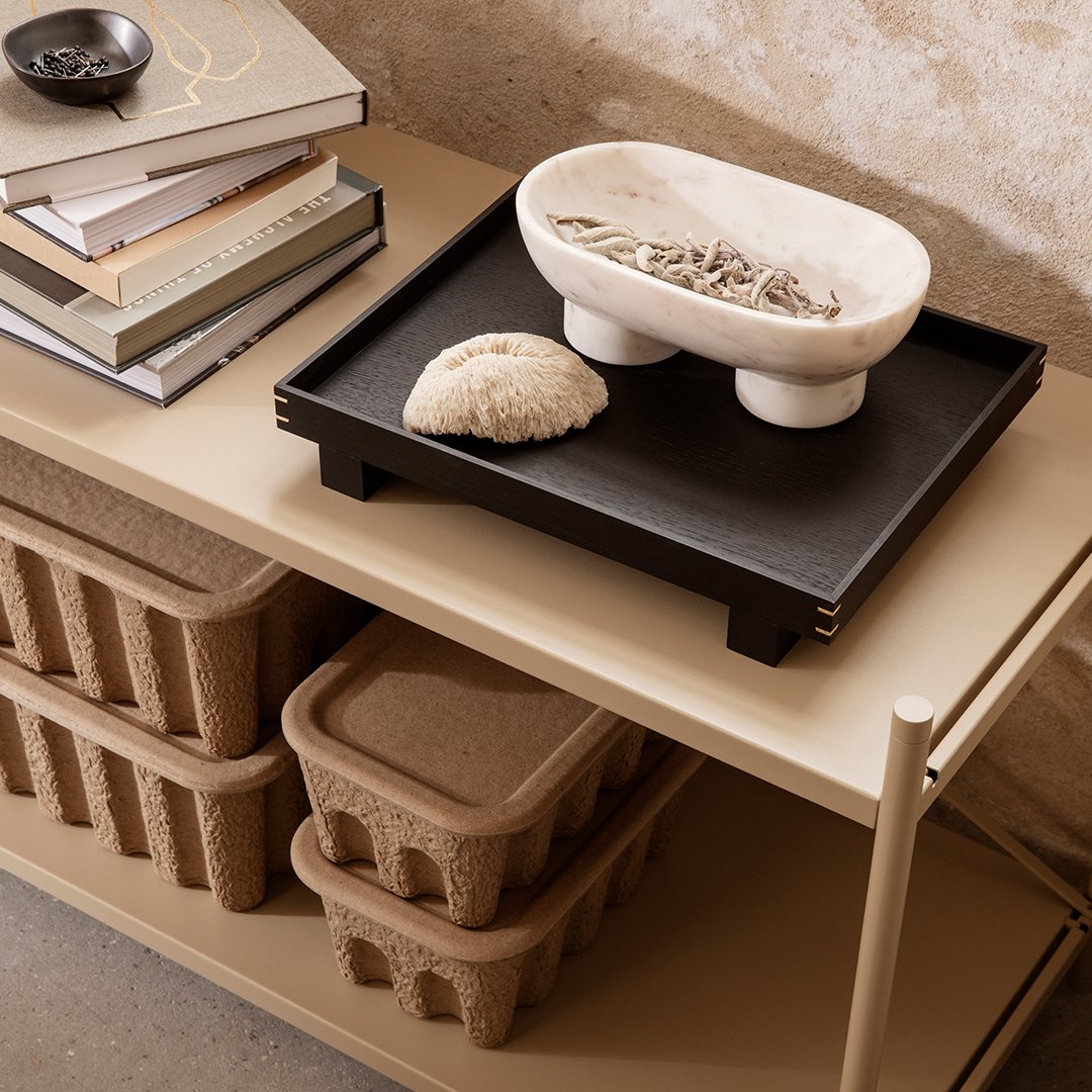 Neutral-toned shelf display with black tray, white bowl, and textured beige storage boxes. Minimalist aesthetic.