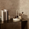 Cream circular organizer with minimalist design, set against a textured stone wall and dark wooden table.