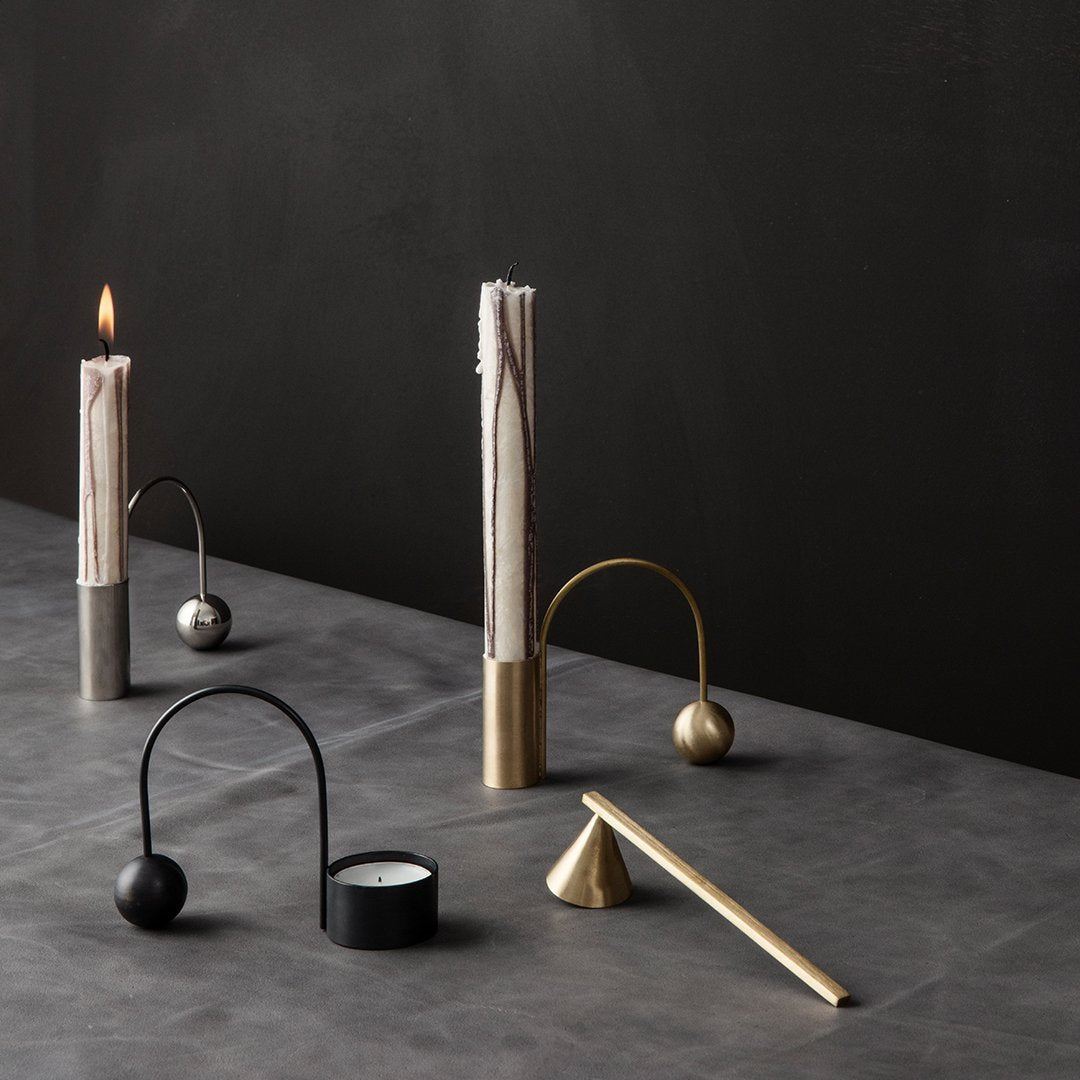 Sleek metal candle holders in gold, silver, and black with elegant curves on a gray tabletop against a dark backdrop.