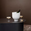 White marble ice bucket with green bottle, set against a dark brown backdrop and sleek black bar with subtle ribbed pattern.