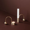 Gold candle holders with curved designs, featuring a white candle and a tea light against a rich brown background.