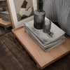 Elegant gray textured fabrics stacked on a wooden tray, complemented by a smoky glass vase and patterned decor.