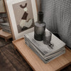Gray textured placemats stacked with a smoky glass vase and cup on a wooden tray, accented by abstract art.