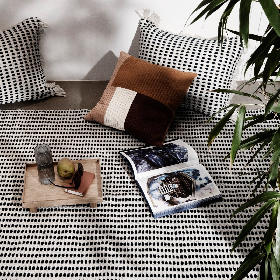 Black and white patterned blanket with brown accent pillows, styled with a tray and magazine on a neutral background.