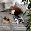 Black and white patterned blanket with brown accent pillows, styled with a tray and magazine on a neutral background.