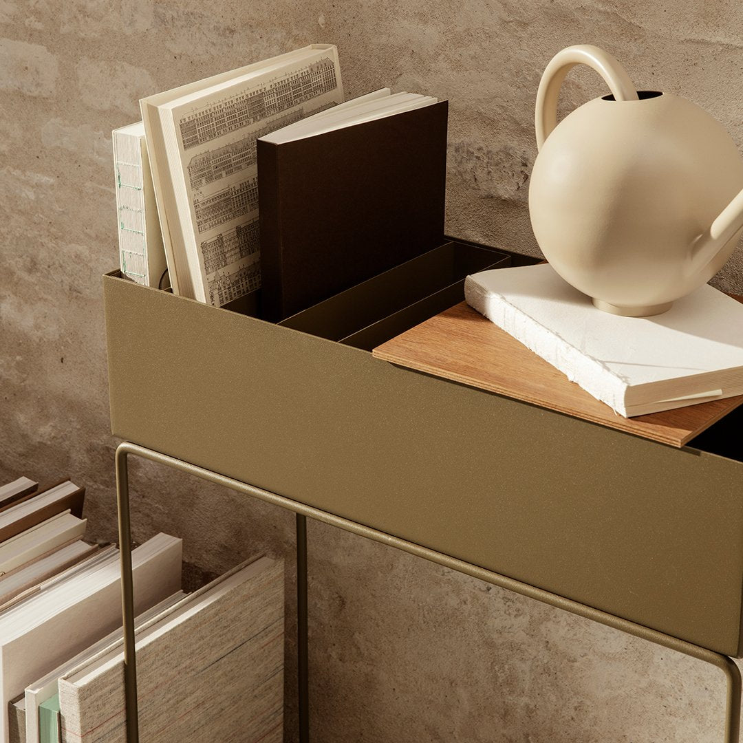 "Olive green storage unit with wooden accents, featuring neutral books and a white ceramic vase on a textured surface."