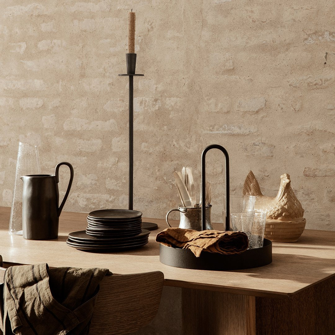 Elegant black dinnerware and candle holder on a rustic wooden table with soft beige textures and natural accents.