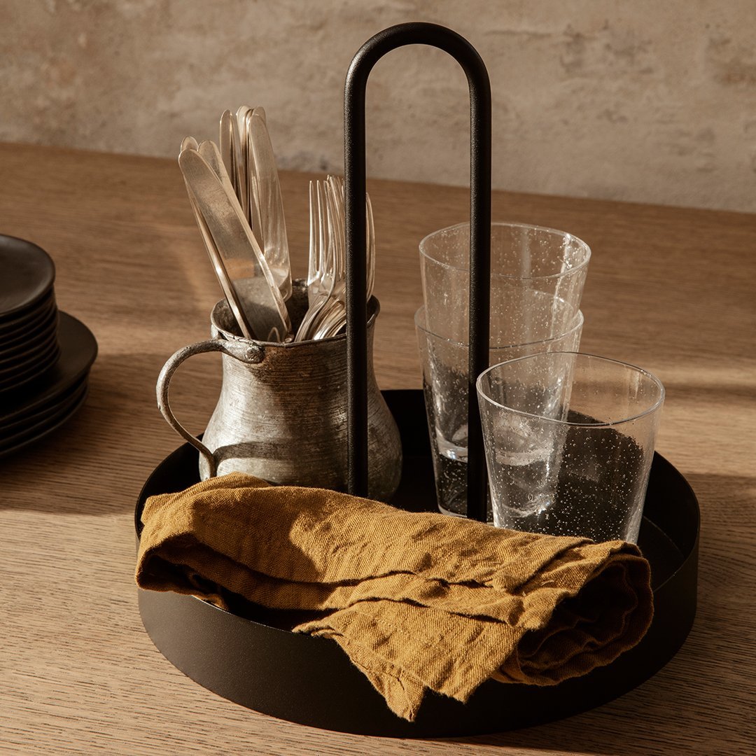 Black serving tray with clear glasses, silver utensils, and a brown linen cloth. Simple, modern design with neutral tones.
