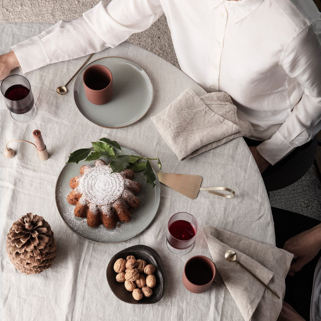 Elegant table setting featuring neutral linens, soft green plates, and rich burgundy drinks, adorned with natural textures.