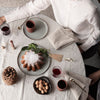 Elegant table setting featuring neutral linens, soft green plates, and rich burgundy drinks, adorned with natural textures.