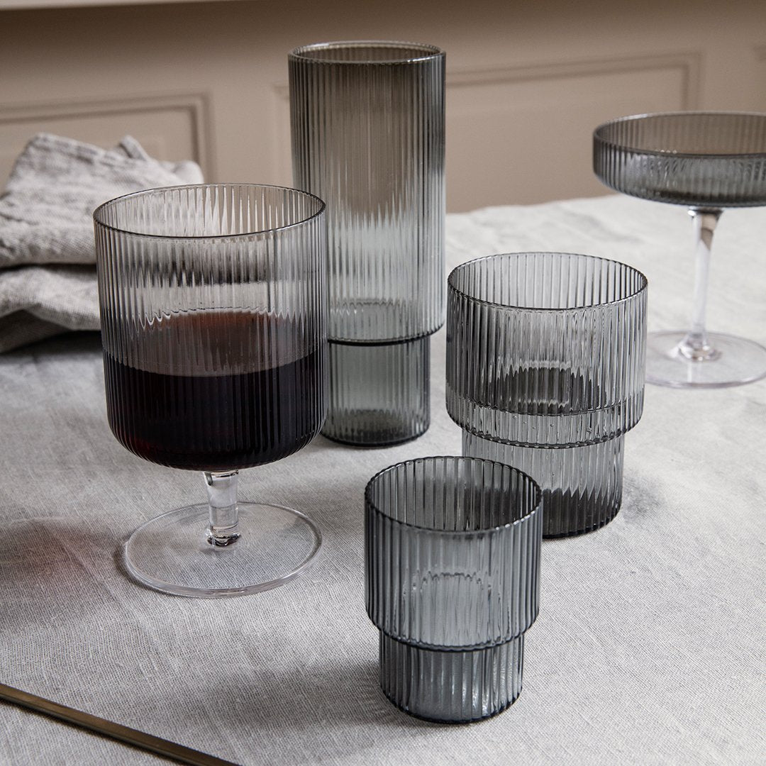 Set of smoky gray glass tumblers with vertical ribbed patterns on a textured tablecloth.