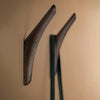 Dark wood wall hooks against a warm beige background, highlighting a smooth, minimalist design.