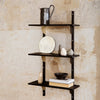 Black metal shelving unit against a textured beige wall, featuring minimalist decor items and a monochrome color palette.