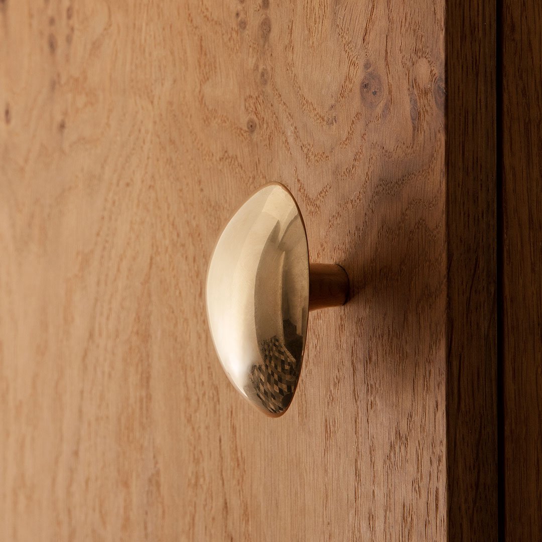 Brass cabinet knob against a textured wooden background, featuring a smooth, curved surface.