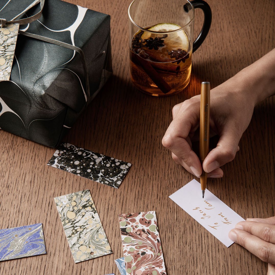 "Colorful patterned gift tags in blues, greens, and neutrals, with a sleek black packaging and wood background."