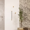 Brass wall hooks against a white wall, paired with a botanical patterned wallpaper in muted greys and greens.