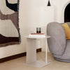 "Modern white side table with sleek lines, paired with a soft gray couch and patterned wall tapestry in warm tones."