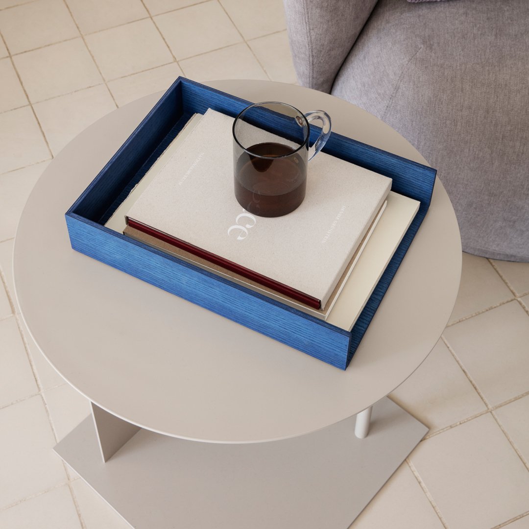 Blue and white tray with patterned books, featuring a dark glass mug on a round beige table.