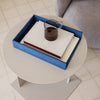 Blue and white tray with patterned books, featuring a dark glass mug on a round beige table.