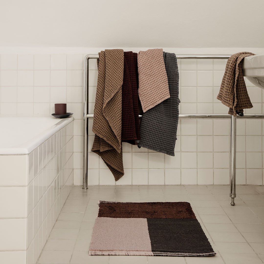 Textured towels in shades of brown, gray, and mauve hanging on a rack, paired with a geometric patterned rug.