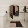 Textured towels in shades of brown, gray, and mauve hanging on a rack, paired with a geometric patterned rug.