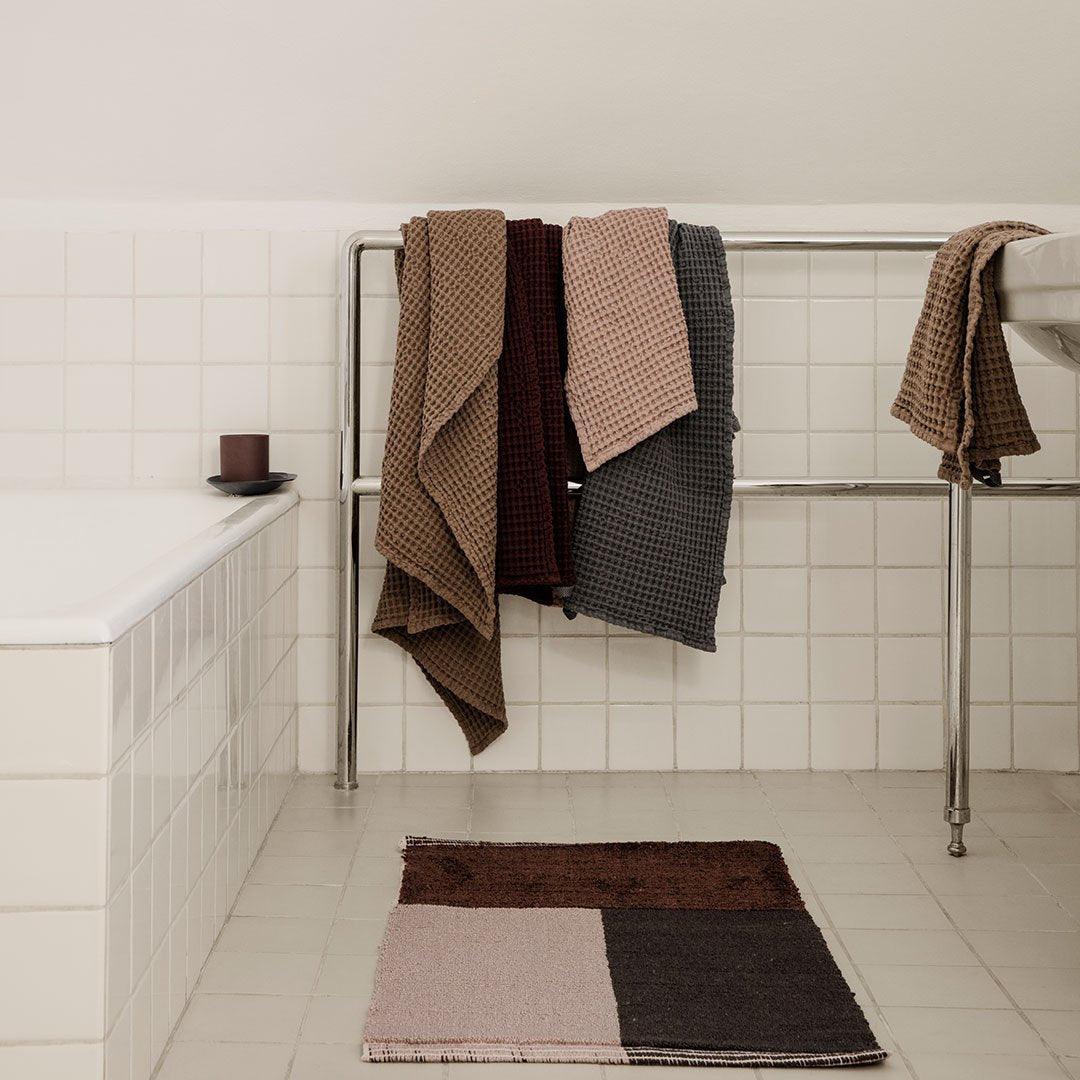 Textured towels in earthy tones of brown, gray, and beige, with a geometric pattern rug in complementary colors.