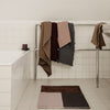 Textured towels in earthy tones of brown, gray, and beige, with a geometric pattern rug in complementary colors.