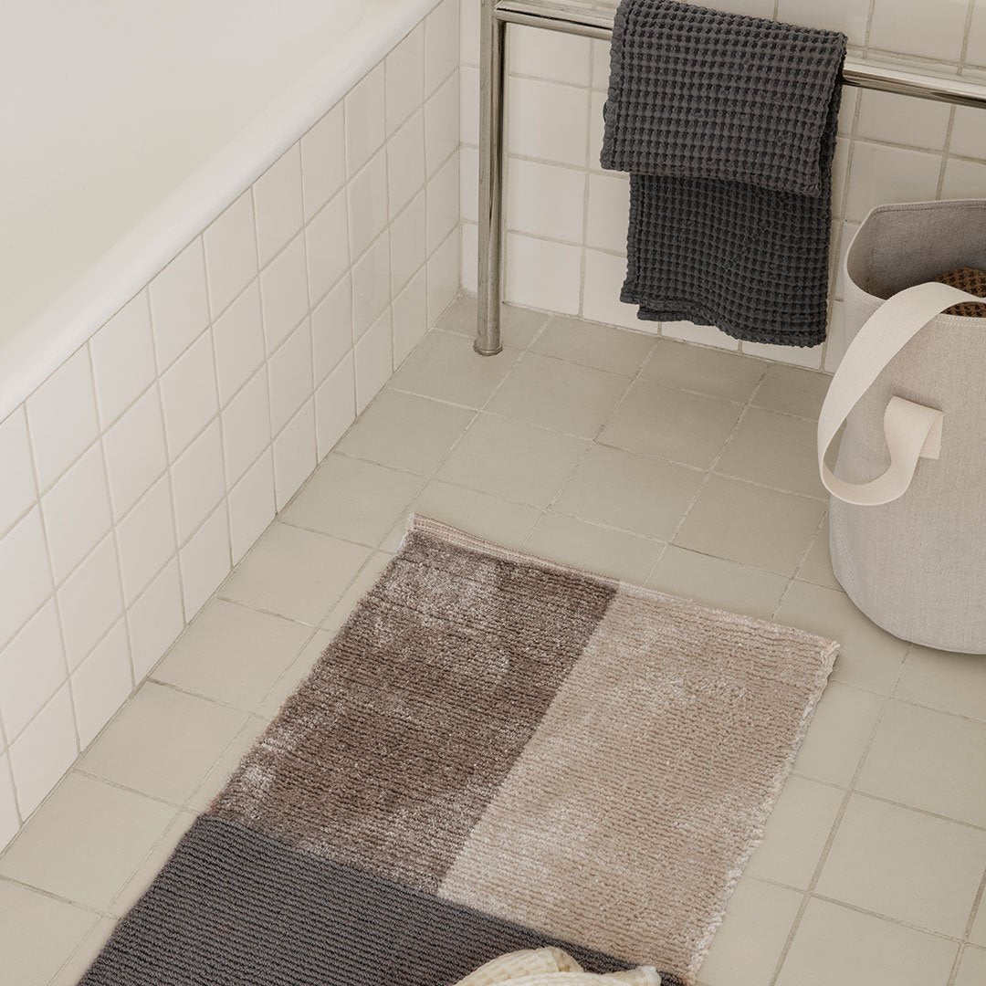 Tan, gray, and beige patterned rug with various textures, placed on a neutral tiled bathroom floor.
