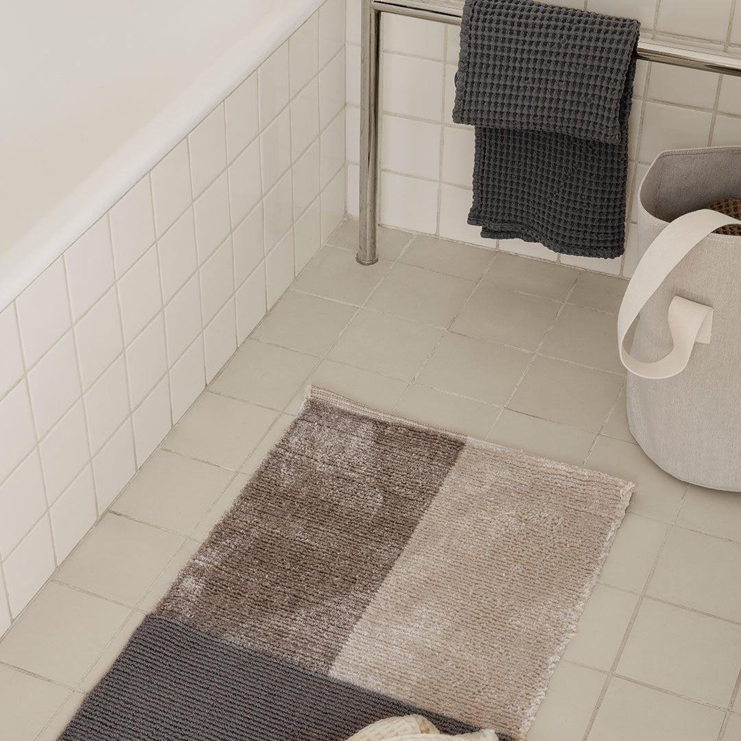 Neutral-toned bath mat featuring a modern abstract pattern in shades of gray and beige.