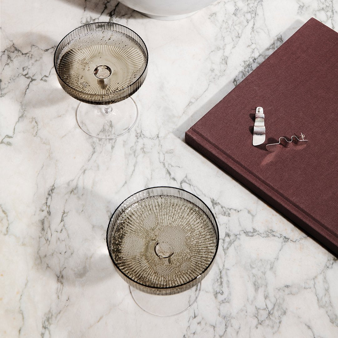 Smoky gray glasses with intricate patterns, marble surface, and a deep burgundy book. Elegant and modern tabletop setting.