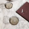 Smoky gray glasses with intricate patterns, marble surface, and a deep burgundy book. Elegant and modern tabletop setting.