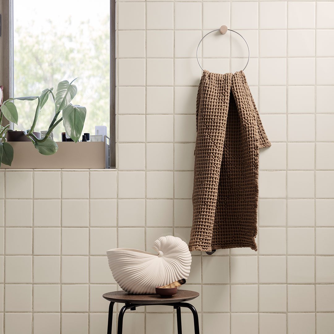 Textured brown waffle-patterned towel hanging on a circular hanger against light-colored tiled wall.