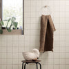 Textured brown waffle-patterned towel hanging on a circular hanger against light-colored tiled wall.