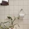 Light green square tiles with a glossy finish, complemented by textured brown towels and lush green plant accents.