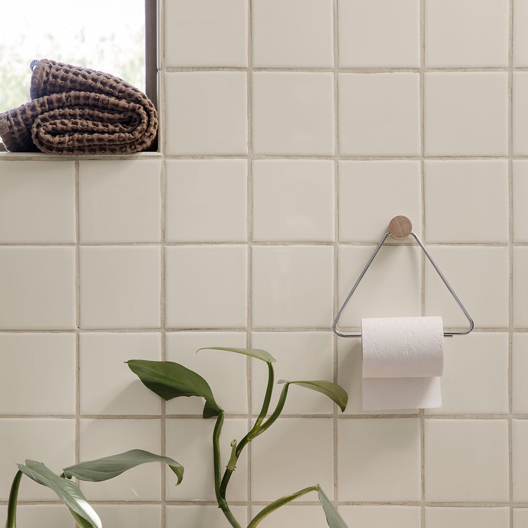 Soft beige tiled wall with a textured pattern, featuring a black and brown woven towel and greenery accent.