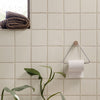 Soft beige tiled wall with a textured pattern, featuring a black and brown woven towel and greenery accent.