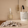 Clear glass soap dispenser, beige cloth with black grid pattern, white woven basket, and neutral background tones.
