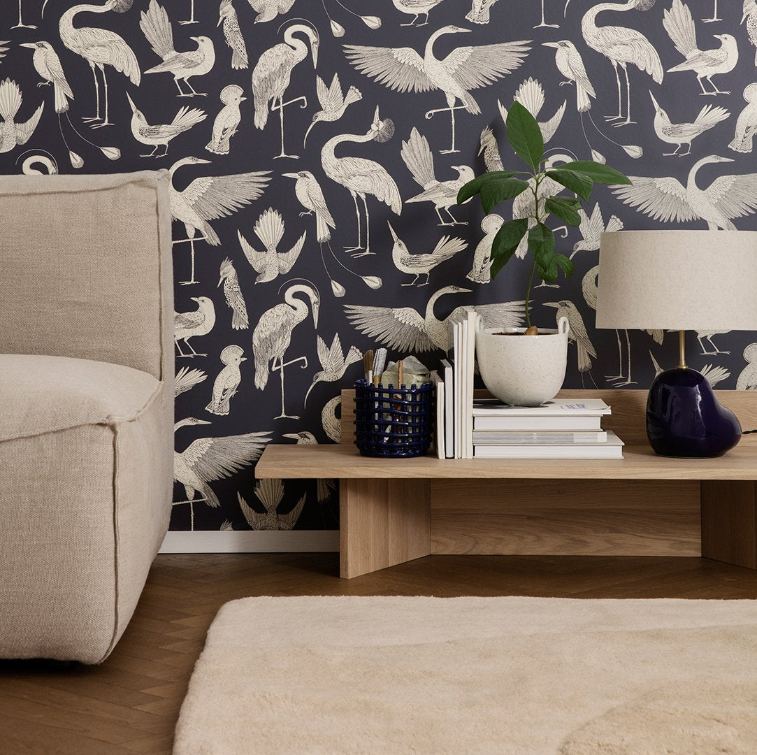 Navy blue wallpaper with white crane and bird patterns, complemented by neutral-toned furniture and decor.