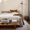 Cozy bed featuring a textured cream quilt, striped orange and brown pillows, and a warm, mustard-colored throw.