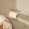 White toilet paper roll with a gold artistic holder against a minimalist beige wall, featuring textured patterns.