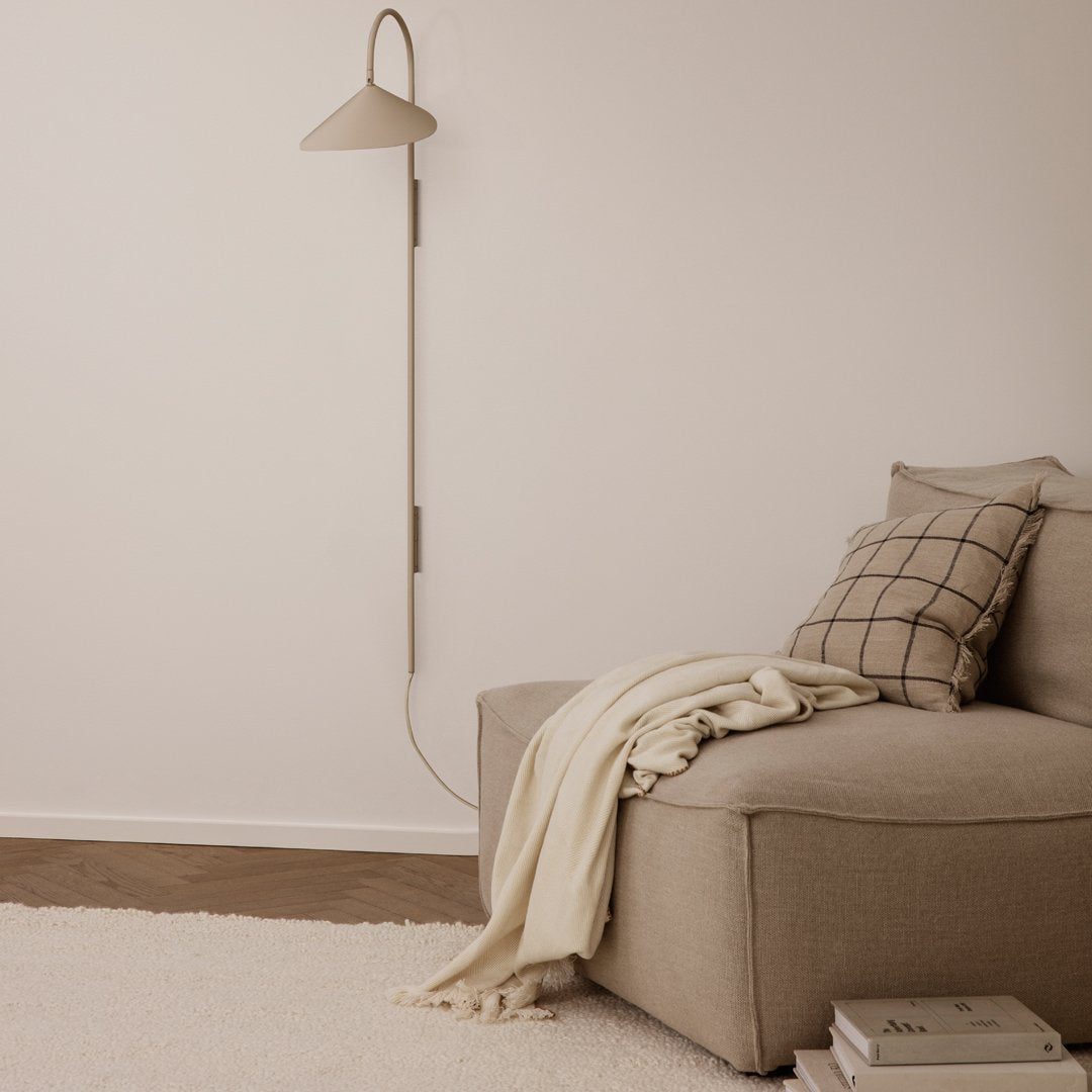 Neutral beige sofa with a checked pillow, complemented by a soft cream throw and a sleek gray wall lamp.