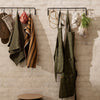 "Collection of green, striped, and checkered aprons and towels hanging against a textured beige wall."