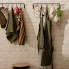 "Assorted aprons and kitchen towels in green, brown, and striped patterns, hanging against a textured wall."