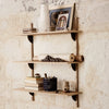 Natural wood shelves with a light finish, accented by black mounting brackets against a textured beige wall.