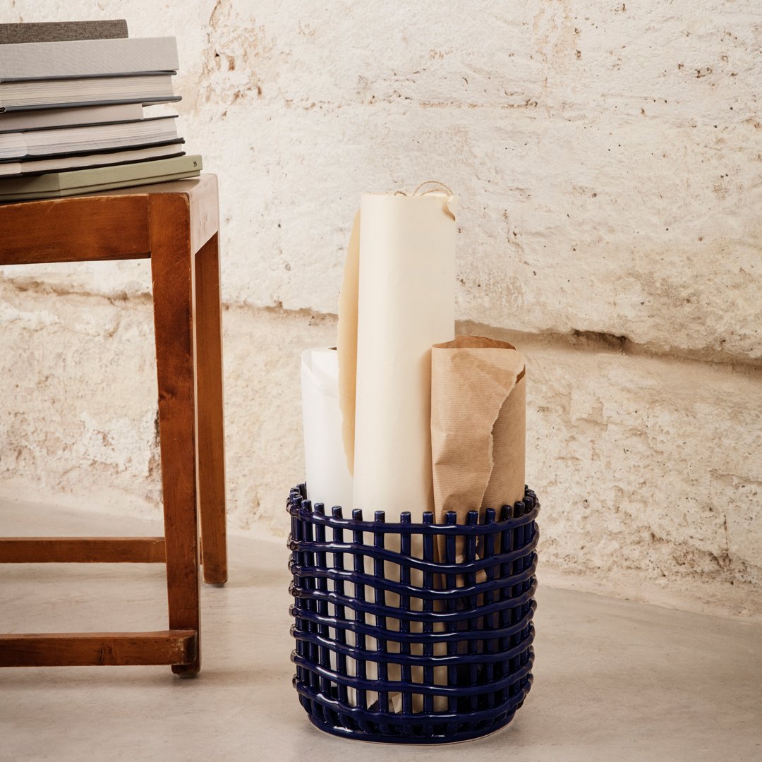 Navy blue woven basket with a geometric pattern, holding rolled papers and wrapped items on a light gray floor.