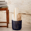 Navy blue woven basket with a geometric pattern, holding rolled papers and wrapped items on a light gray floor.